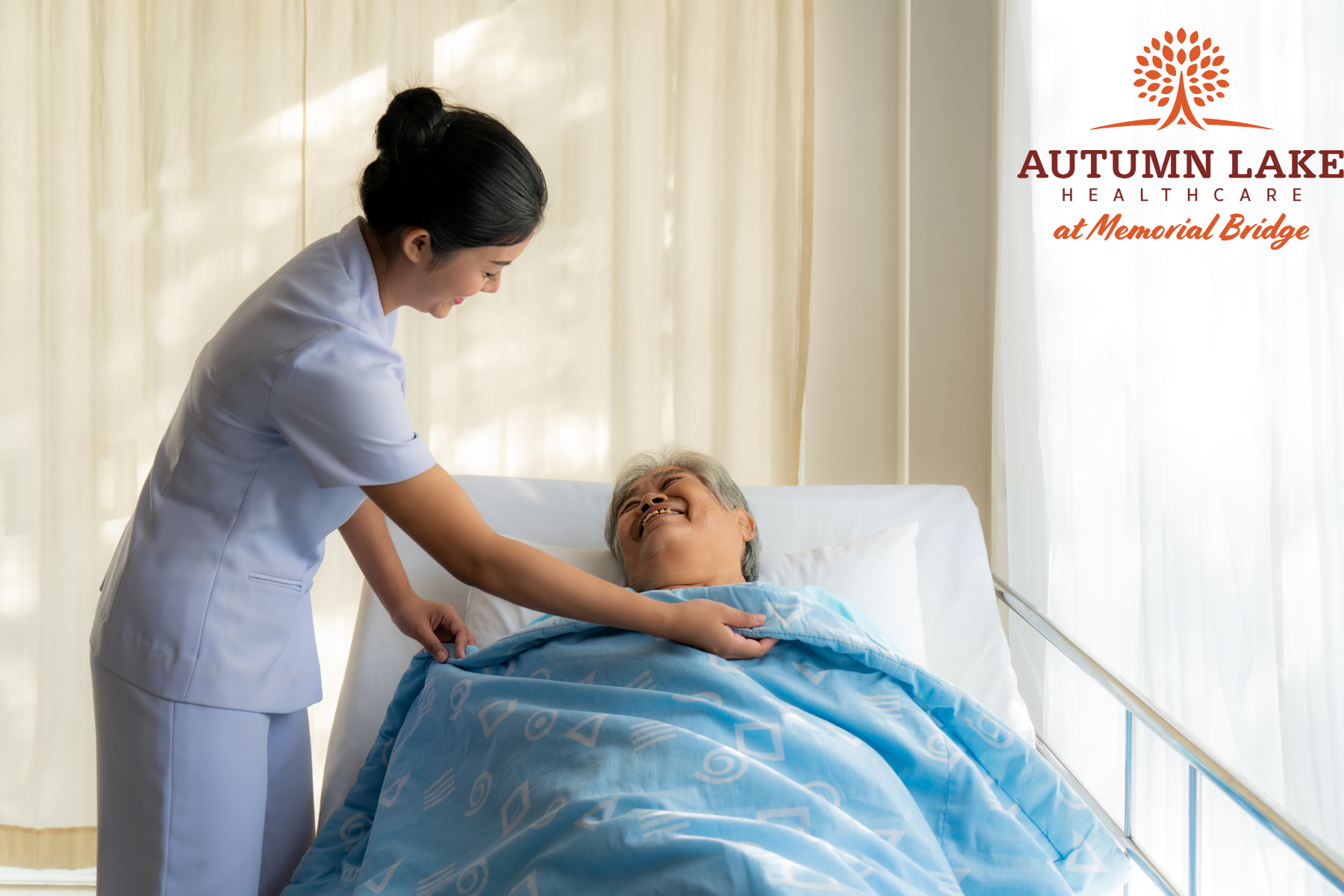A caregiver at Autumn Lake Healthcare smiles while adjusting a blanket for a senior resident in bed.