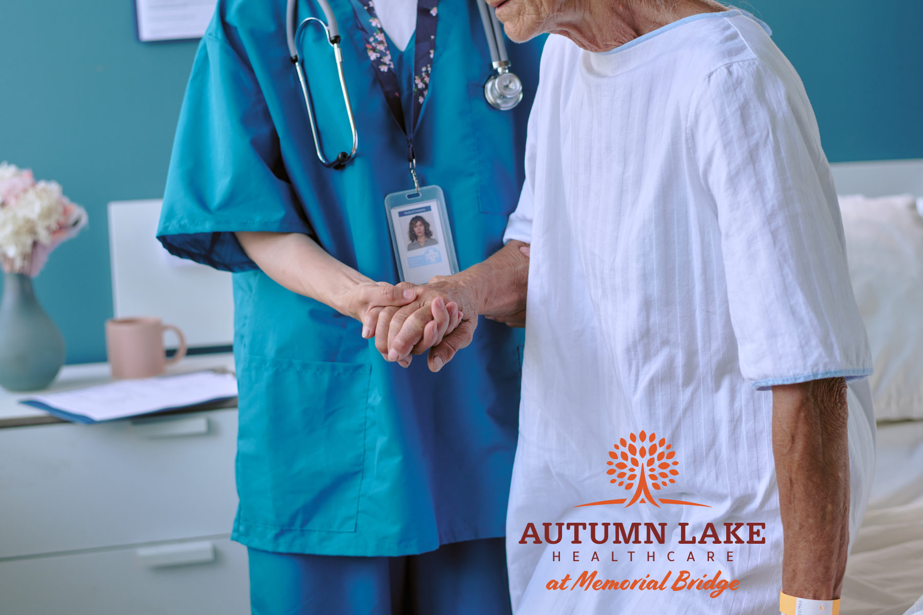 A nurse in blue scrubs gently holds the hand of an elderly patient in a hospital gown.